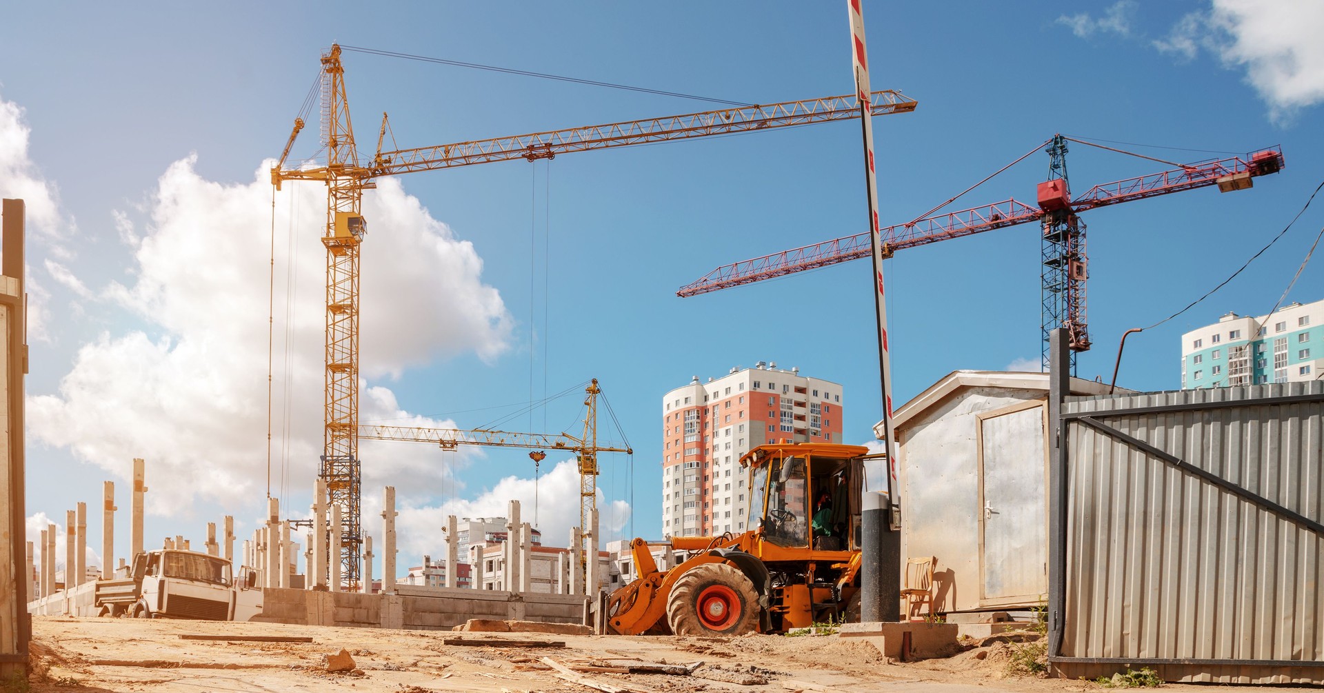 open steel gate on dirty construction site with yellow crane and tractor